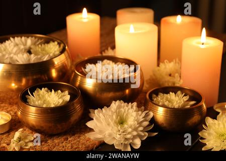 Ciotole tibetane con acqua, bellissimi fiori e candele brucianti sul tavolo Foto Stock
