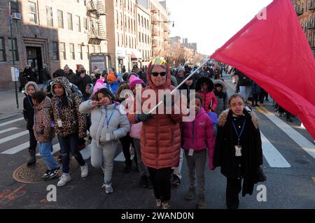 New York City, Stati Uniti. 5 gennaio 2024. Un partecipante alla parata che indossa una corona giocattolo e regge una bandiera rossa, conduce un gruppo di studenti lungo il percorso della parata durante l'annuale sfilata del Three Kings Day. I festeggiatori si sono riuniti per commemorare la 47a parata annuale del Three Kings Day di El Museo del Barrio nel quartiere East Harlem di New York City. La sfilata celebra il giorno in cui i "tre saggi" hanno portato doni a Gesù dopo la sua nascita. (Foto di Jimin Kim/SOPA Images/Sipa USA) credito: SIPA USA/Alamy Live News Foto Stock