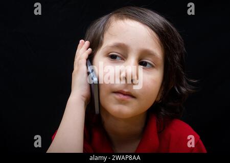 Little Boy tenere lo smartphone come moderna comunicazione mobile gadget Foto Stock