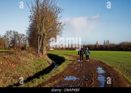 Una coppia più anziana cammina mano nella mano lungo una pista fangosa accanto agli alberi e un ruscello vicino a Cusworth Hall, Doncaster, South Yorkshire. Foto Stock