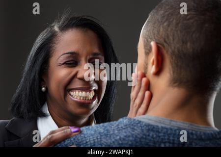 La donna nera in abito da lavoro ride di cuore con un giovane uomo in maglione casual Foto Stock