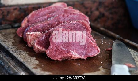 Vista dall'alto di un tagliere ricoperto da una selezione di carne cruda, tra cui bistecca, maiale e pollo, con un coltello affilato posizionato sopra Foto Stock