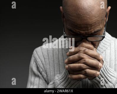 Pregare dio per il perdono l'uomo caraibico che prega con sfondo grigio nero con la gente stock immagine foto stock Foto Stock