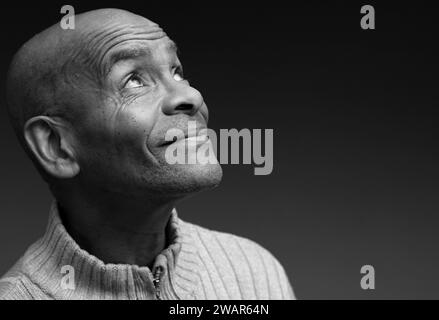 Pregare dio per il perdono l'uomo caraibico che prega con sfondo grigio nero con la gente stock immagine foto stock Foto Stock