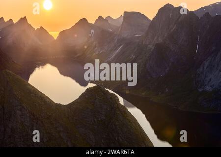 Il sole di mezzanotte proietta un bagliore nebbioso su Reinebringen, con picchi ripidi che incorniciano le acque calme sottostanti, creando un contrasto incredibile nel cuore di lo Foto Stock