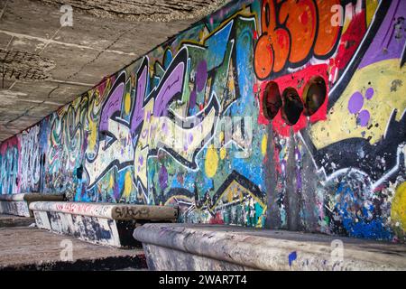 Graffiti colorati dipinti a spruzzo su una parete urbana in un tunnel sotterraneo di giorno Foto Stock