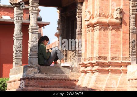 og ragazza usa il telefono e siediti sull'edificio. L'area storica di Bhaktapur e piazza durbar sono un patrimonio vivente in cui la gente vive ancora Foto Stock