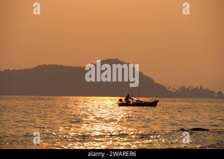 Una barca a vela è sagomata contro un tramonto mozzafiato sull'ampio oceano aperto Foto Stock