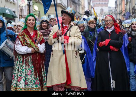 Una folla che indossa corone di carta segue un uomo con una stella mentre partecipa a uno spettacolo di presepe pubblico eseguito sulla strada della città vecchia di Cracovia, in Polonia, il 6 gennaio 2024. Il 6 gennaio è la festa dei tre Re polacchi, quando si svolgono le celebrazioni di massa e il Presepe Play viene eseguito dagli attori insieme ai membri del pubblico. Le celebrazioni hanno il carattere di un festival per famiglie. Oltre 800 città e città hanno eseguito lo spettacolo in Polonia quest'anno. Centinaia di persone hanno partecipato al festival nonostante il freddo e le piogge. Foto Stock