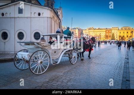 CRACOVIA, POLONIA - 27 DICEMBRE 2023: Carrozza trainata da cavalli durante il periodo natalizio. La piazza principale è circondata da storiche case cittadine (kamienice) e. Foto Stock