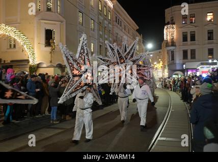 Dreikönigsingen und Glöcklerlauf am Rathausplatz in Gmunden, im oberösterreichischen Salzkammergut, AM 05.01.2024. Sowohl das Dreikönigssingen als auch der Glöcklerlauf sind alte, eingeprägte Brauchtumsveranstaltungen im Salzkammergut in Österreich. während des Glöcklerlaufs tragen junge Burschen prächtig geschmückte Laternenkappen mit meist lokalen Motiven am Kopf. Dabei wird durch laufen, springen und tanzen, mit an Gürteln der Weiß Gekleideten angebrachten Glocken, entsprechend Lärm gemacht und dazu gesungen Damit treiben die Glöckler in der letzten Rauhnacht der Saison, dem 5,1. eines jede Foto Stock