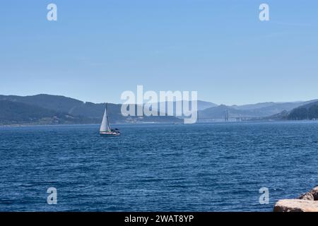 Una bella immagine di una barca a vela che naviga grazie al vento nel Ría de Vigo con il ponte di Rande come testimone Foto Stock