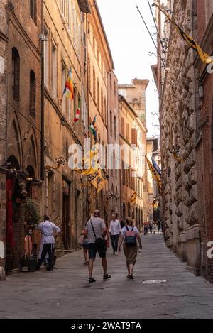 I turisti che camminano attraverso la via di città nel centro storico di Siena, Italia Foto Stock