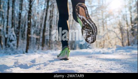 Suola da running immagine ravvicinata dei piedi da jogger invernali nelle sneakers da running sul sentiero innevato del parco durante la giornata di sole. Immagine della suola per la visione posteriore. Foto Stock