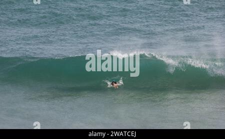 Donna in costume da bagno che si tuffa nel surf a Kynance Cove, Cornovaglia. Kernow Foto Stock