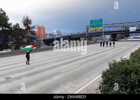 Seattle, Washington, USA. 6 gennaio 2024. Un uomo sventola la bandiera della Palestina mentre il dipartimento di polizia di Seattle si avvicina ai manifestanti che hanno bloccato la i-5 in direzione nord in solidarietà con la Palestina. Le proteste settimanali che chiedono un cessate il fuoco immediato sono aumentate dallo scoppio della guerra tra Israele e gruppi militanti palestinesi guidati da Hamas nella Striscia di Gaza in ottobre. Credito: Paul Christian Gordon/Alamy Live News Foto Stock