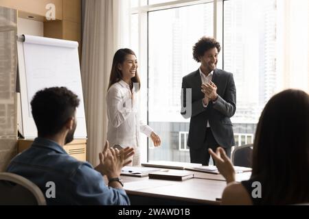 Entusiasta colleghi eterogenei e allegri applaudendo una donna professionale asiatica di successo Foto Stock