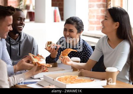 Sorridenti studenti multietnici si divertono a gustare una pausa pranzo con pizza Foto Stock