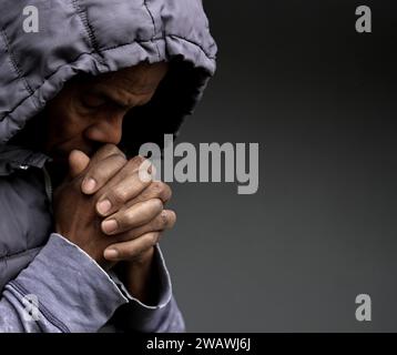 Pregare dio per il perdono l'uomo caraibico che prega con sfondo grigio nero con la gente stock immagine foto stock Foto Stock