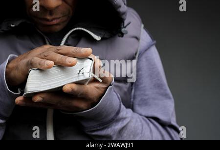 Pregare dio per il perdono l'uomo caraibico che prega con sfondo grigio nero con la gente stock immagine foto stock Foto Stock