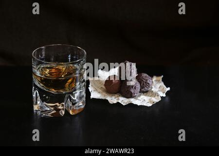 Bicchiere di brandy e tartufi di cioccolato su carta su sfondo scuro con spazio per la copia Foto Stock