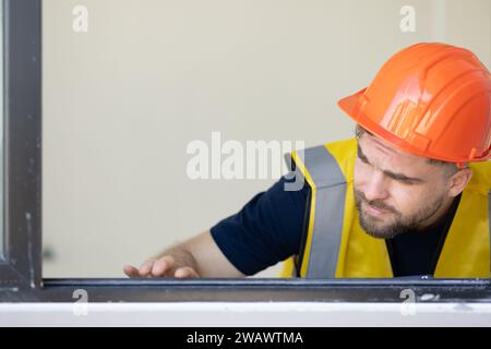 Il giovane muratore edile guarda un livello preciso di telaio delle finestre per dettagli di alta precisione e qualità per il lavoro di costruzione Foto Stock