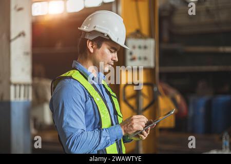 professionista adulto ingegnere senior uomo ufficiale in uniforme di sicurezza che guarda lo schermo di un tablet in officina industriale. Foto Stock