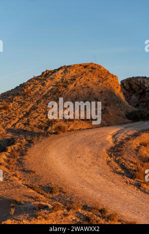 Strada sterrata in un arido paesaggio desertico con scogliere lontane al tramonto, Elche, provincia di Alicante, Spagna - foto di magazzino Foto Stock