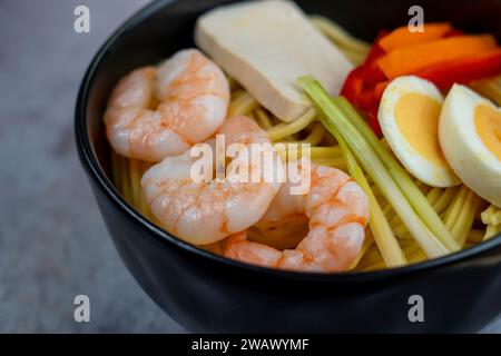 Friggete gli spaghetti con verdure e gamberetti in un recipiente nero. Sfondo ardesia. Vista dall'alto. Copia spazio. con ingredienti uova, tofu, gamberi Foto Stock