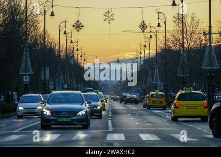 Budapest, Ungheria - 16 dicembre 2023: Vista da Piazza degli eroi, vista su via Andrassy con la luce dorata del tramonto. Il traffico della macchina in primo piano. Foto Stock