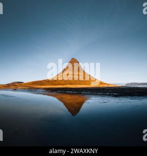 Splendida vista aerea dell'alta montagna Kirkjufell in Islanda, sulla penisola di Snaefellsnes. Alba al tramonto con luce arancione tenue. Islanda occidentale. Foto Stock