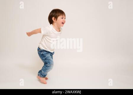 Il bambino corre e salta, sfondo bianco studio. Buon bambino che corre a tutta lunghezza con un sorriso sul viso Foto Stock