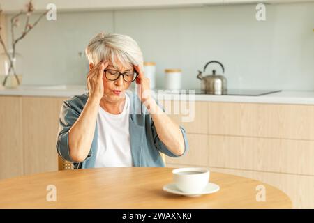 Mal di testa. Donna anziana infelice di mezza età che soffre di mal di testa malata che sfrega le tempie a casa. Anziana nonna anziana matura che tocca i templi che sperimenta stress donna che sente dolore alla testa Foto Stock