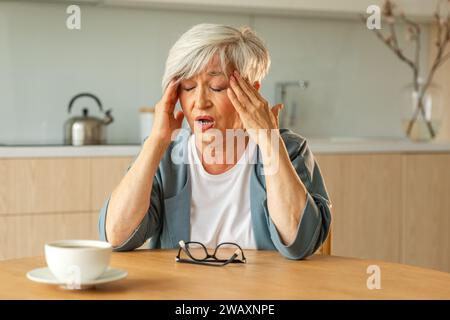 Mal di testa. Donna anziana infelice di mezza età che soffre di mal di testa malata che sfrega le tempie a casa. Anziana nonna anziana matura che tocca i templi che sperimenta stress donna che sente dolore alla testa Foto Stock