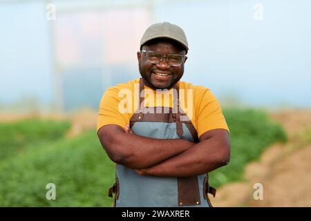 Primo piano di un contadino nero in una serra, colture sullo sfondo, sorridendo. Foto Stock