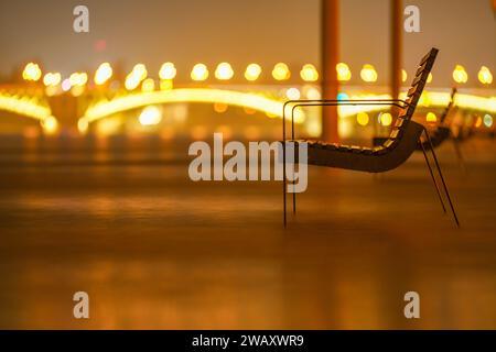 Budapest, Ungheria - 29 dicembre 2023: Fiume Danubio allagato. Panchina vicino all'edificio del parlamento. Ponte Margit sullo sfondo. Foto Stock