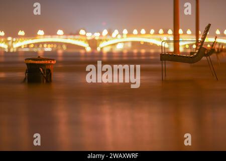 Budapest, Ungheria - 29 dicembre 2023: Fiume Danubio allagato. Panchina vicino all'edificio del parlamento. Ponte Margit sullo sfondo. Foto Stock