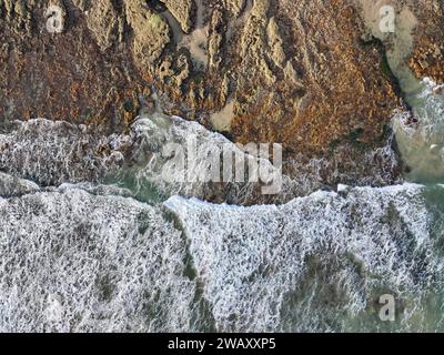 Una tranquilla spiaggia con grandi onde che si infrangono su una costa rocciosa Foto Stock