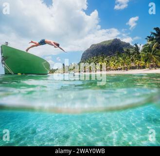 Salta un ragazzo adolescente da una barca di legno per fare snorkeling nella laguna turchese pulita sulla spiaggia delle palme di le Morne con il monte le Morne Brabant. Isola di Mauritius. Foto Stock