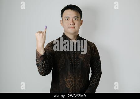 L'uomo asiatico che indossa un panno Batik mostra il suo piccolo dito con inchiostro viola applicato dopo le elezioni presidenziali indonesiane o di Pemilu Foto Stock