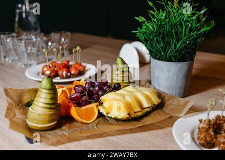 Vassoio di frutta elegantemente organizzato con pere affettate, kiwi, arancia, ananas e uva su un tavolo di legno. Foto Stock