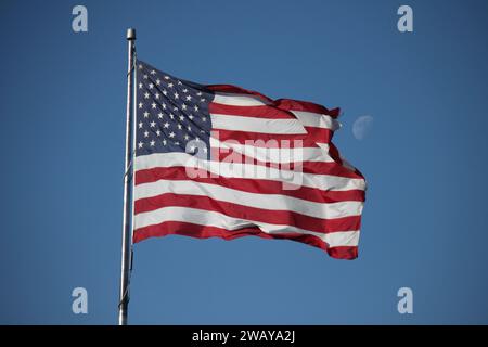 American Flag soffia nel vento con la luna in primo piano dietro di essa durante il giorno Foto Stock