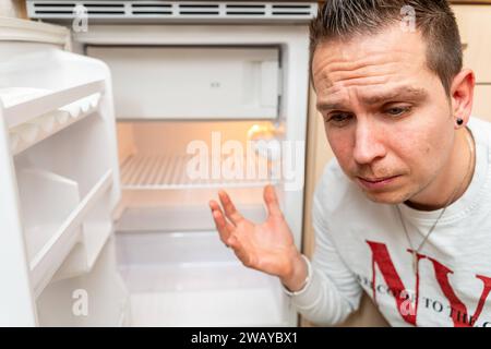 Baviera, Germania - 6 gennaio 2024: Un uomo triste davanti a un frigorifero vuoto, inflazione e povertà concetto *** Ein trauriger Mann vor einem leeren Kühlschrank, Inflation und Armut Konzept Foto Stock