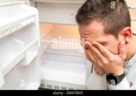 Baviera, Germania - 6 gennaio 2024: Un uomo triste davanti a un frigorifero vuoto, inflazione e povertà concetto *** Ein trauriger Mann vor einem leeren Kühlschrank, Inflation und Armut Konzept Foto Stock