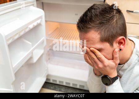 Baviera, Germania - 6 gennaio 2024: Un uomo triste davanti a un frigorifero vuoto, inflazione e povertà concetto *** Ein trauriger Mann vor einem leeren Kühlschrank, Inflation und Armut Konzept Foto Stock