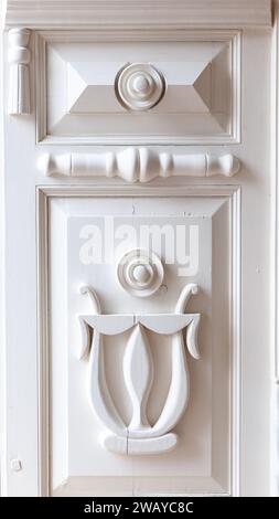 Frammento di porte in legno antico intagliato bianco con motivi e arpa. Foto Stock