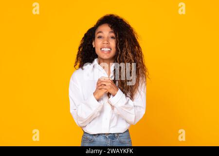 Donna nera sorridente che tiene per mano insieme implorando su sfondo giallo Foto Stock