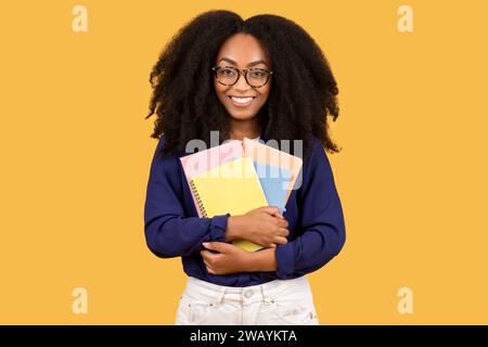 Giovane donna nera studiosa con occhiali e quaderni colorati Foto Stock