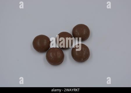 Cioccolatini, arachidi, noci, uva passa ricoperta di glassa al cioccolato, ciottoli di cioccolato disposti su sfondo bianco. Foto Stock