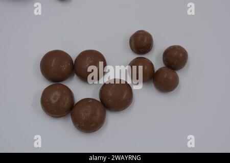 Cioccolatini, arachidi, noci, uva passa ricoperta di glassa al cioccolato, ciottoli di cioccolato disposti su sfondo bianco. Foto Stock